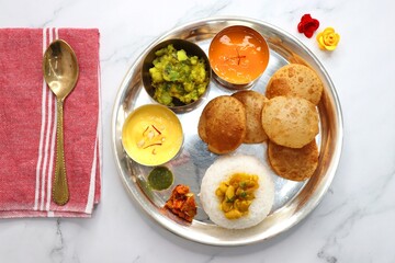 Indian vegetarian Thali or platter includes Aloo ki sabji, dal rice, Puri bhaji, Shrikhand or Srikhand, Aamras, papad, pickle, and chutney. Mashed potato curry or masala. Indian Festival food Thali.