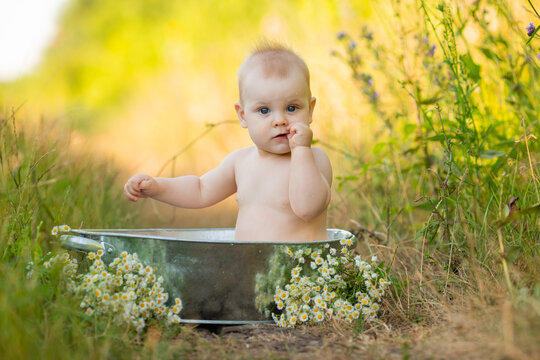 cute baby is bathing in an iron basin in the garden. outdoor water treatments