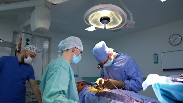Surgeon does the precise work at operation using tools in both hands. Helping assistants standing beside the patient.