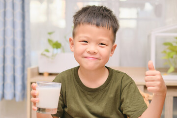 Cute Asian 5 years old kindergarten boy child drinking milk from a glass, Little kid sitting and...
