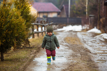 Little boy in protective rubber boots and rain clothes jumping in mud puddle. Happy child having...