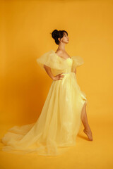 Fototapeta premium Profile portrait of a beautiful middle-aged woman in a yellow dress, her hair pulled up against a yellow background