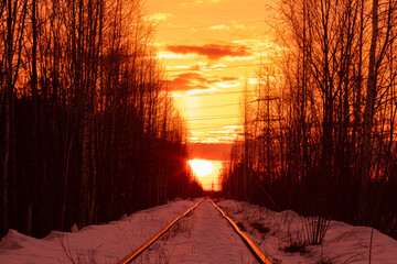 Beautiful vivid colorful and bright winter landscape of old neglected railway among forest trees with yellow and orange sunset or sunrise sky