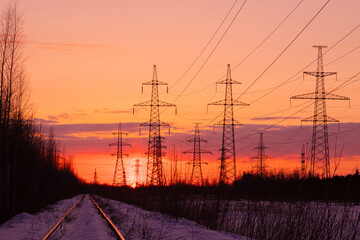 The towers of electric main in the countryside near old railway on the background red, orange and...