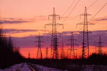 The towers of electric main in the countryside near old railway on the background red, orange and yellow sunset or sunrise sky