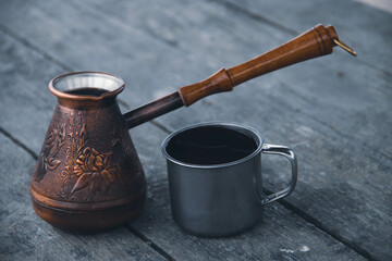 
Copper cezve and a metal mug with coffee on a wooden table.