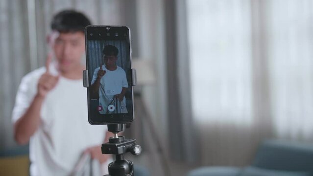 Display Smartphone Of Asian Boy Shows Trick With Disappearing On Mobile Phone Camera While Recording Video Content For Social Networks In Cozy Room
