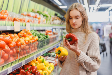 Woman holds red and yellow bell pepper in supermarket. Grocery farm store