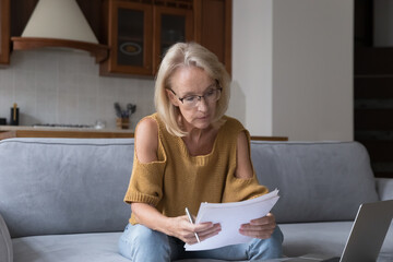 Serious mature 50s landlady woman un glasses reading domestic papers, insurance, mortgage...