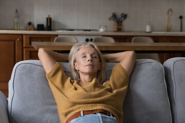 Calm peaceful elder lady relaxing with closed eyes on comfortable sofa at home, taking deep breath...