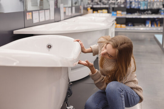 Woman Choosing New Acrylic Bathtub In Hardware Store. Home Bathroom Renovation Concept