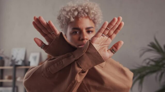 Young pretty African American woman demonstrates stop gesture showing crossed arms calls to solve problem in society fight against discrimination, focus on hands. Feminism, canceling concept.
