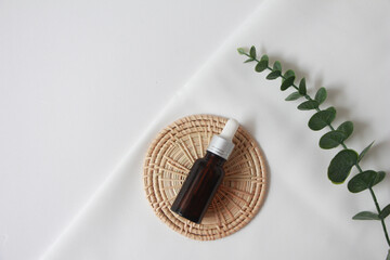 Dropper bottle serum on wood plate. Natural facial essential oil or serum packaging on white fabric background. Beauty product branding mock-up.  Cosmetic skincare concept. top view
