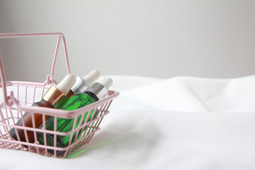 Fototapeta na wymiar dropper bottle serum on pink basket. Natural facial essential oil or serum packaging on white fabric background. Beauty product branding mock-up. Cosmetic skincare concept.