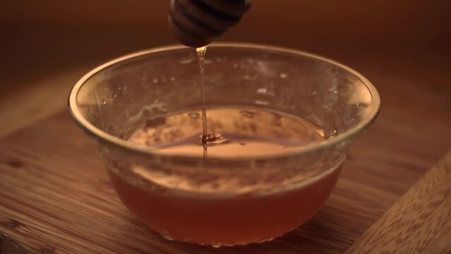 thick natural honey is poured from a wooden spoon into a glass plate.Close-up