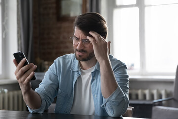 Concerned annoyed smartphone user man staring at cellphone screen with upset face, having problems...