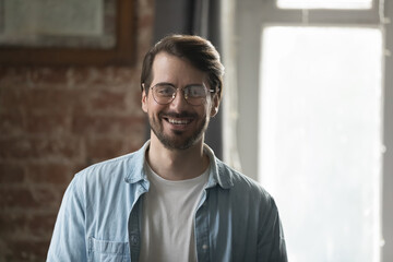 Happy confident millennial business professional man in glasses head shot portrait. Cheerful handsome young startup leader, company founder posing in loft office, looking at camera, smiling