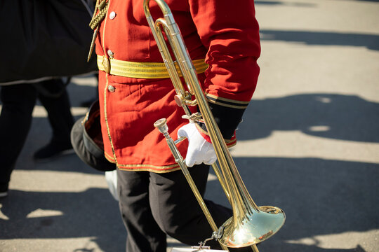 Orchestra member holds brass pipe. Trumpeter details. Ceremonial red uniform.