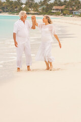 Retired Caucasian couple in white clothes dancing on a Caribbean beach