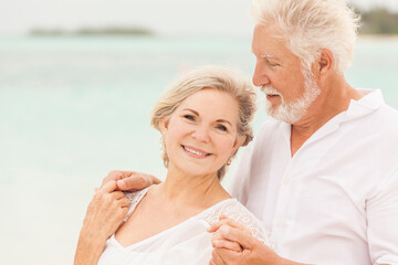 Smiling portrait of senior Caucasian couple in white clothes on a beach vacation