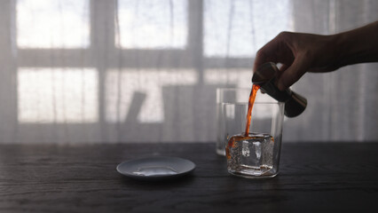 pour orange syrup over ice ball in tumbler glass on wood table
