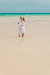 Fototapeta na wymiar Senior Caucasian couple in casual white clothes sharing kiss on a tropical beach