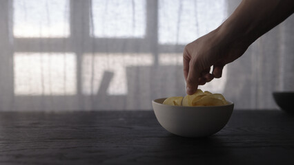 man hand take potato chips from white bowl on oak table