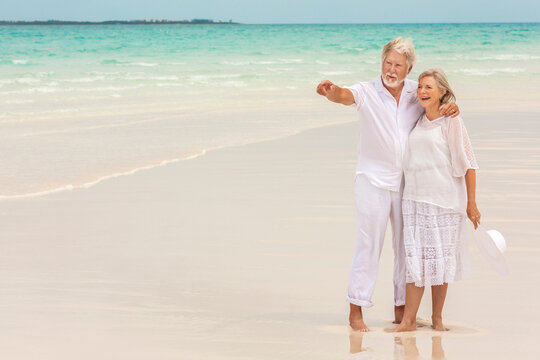 Barefoot Caucasian senior couple in white clothes on a travel resort beach
