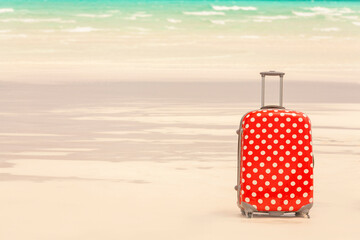 Colorful polka dot travel suitcase on a white sand beach