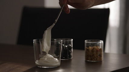 making granola with yogurt in tumbler glass on wood table