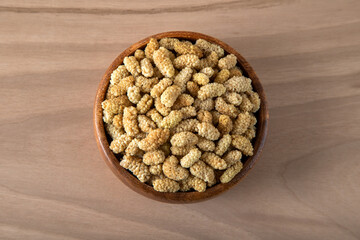 Bowl full of dried mulberry on a wooden background