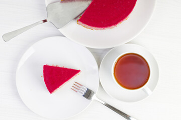 Closeup homemade raspberry and strawberry cheesecake and cup of tea on white wooden table. Top view.
