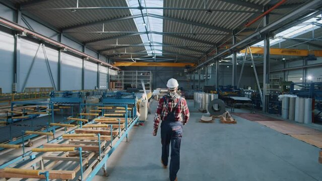 Shot back man engineer wearing safety uniform and hard hat walking checks production processes in factory. Look around. Inspector in warehouse.
