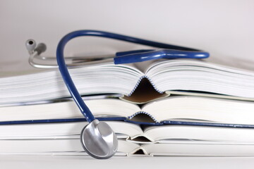 Blue stethoscope and stack of opened books isolated on white background. Medical professional education and information concept.