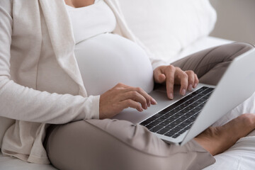Late pregnant woman using laptop computer, consulting doctor online, typing, resting on bed....