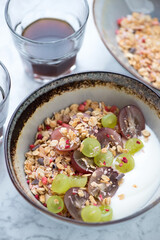 Bowl with granola, greek yogurt, red and green grapes, vertical shot, close-up