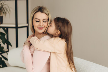 Close-up portrait of mother and little daughter. The girl smiles and hugs her mother