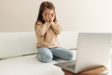 scared little girl closing face with hands looking at laptop screen