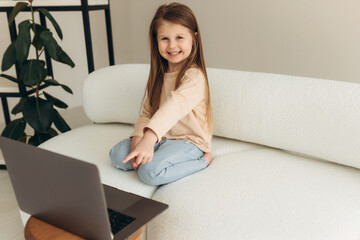 addicted to modern technology, joyful little cute girl sitting on the couch with a computer,...