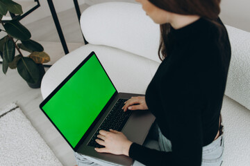 Over the Shoulder: Creative Young Woman Sitting at Her Desk Using Laptop with Mock-up Green Screen. Office where Diverse Team of Young Professionals Work on Computers.