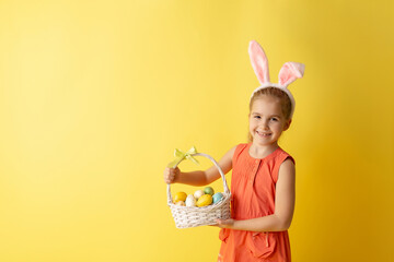 Beautiful cute little girl in Easter bunny ears smiling and holds spring bouquet of tulips on a yellow background