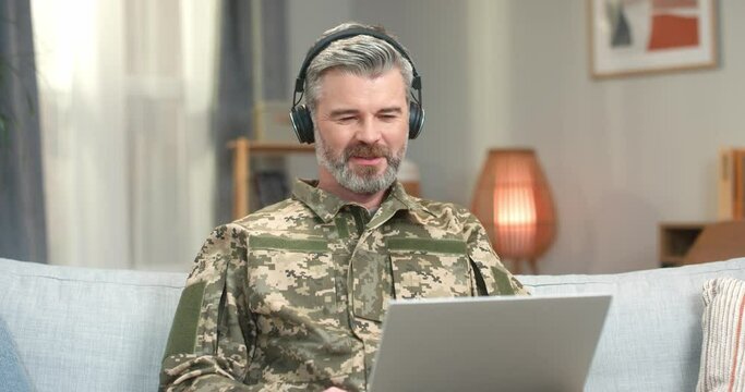 Caucasian soldier sitting on sofa ans typing on laptop