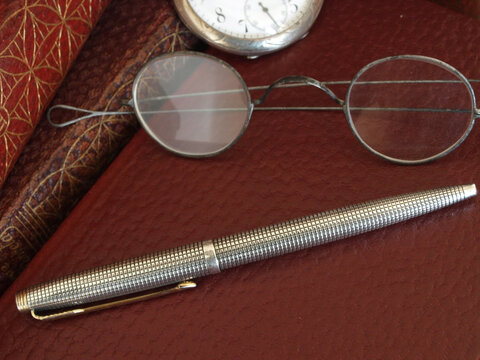 vintage silver ballpen, glasses and pocket watch over red leather books