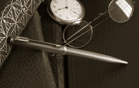 classic silver pen, glasses and pocket watch over red leather cover books