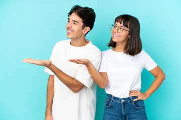 Young mixed race couple isolated on blue background pointing back and presenting a product