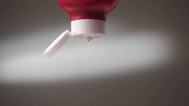 Ketchup being squeezed out of bottle. Close-up of jet of red ketchup on gray background. Ketchup spills out of large red bottle