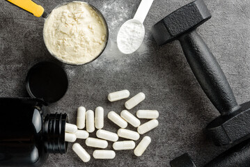 The concept of sports supplements and nutrition. Scoops with protein and creatine, capsules and...