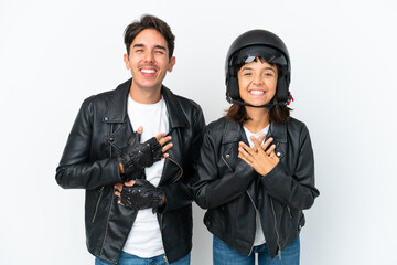 Young mixed race couple with a motorcycle helmet isolated on white background smiling a lot while putting hands on chest