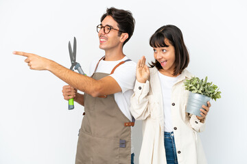 Young mixed race gardeners holding a plant and pruning shears isolated on white background pointing...
