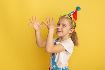 Funny kid clown against yellow background. Happy child playing with festive decor. Birthday and 1 April Fool's day concept